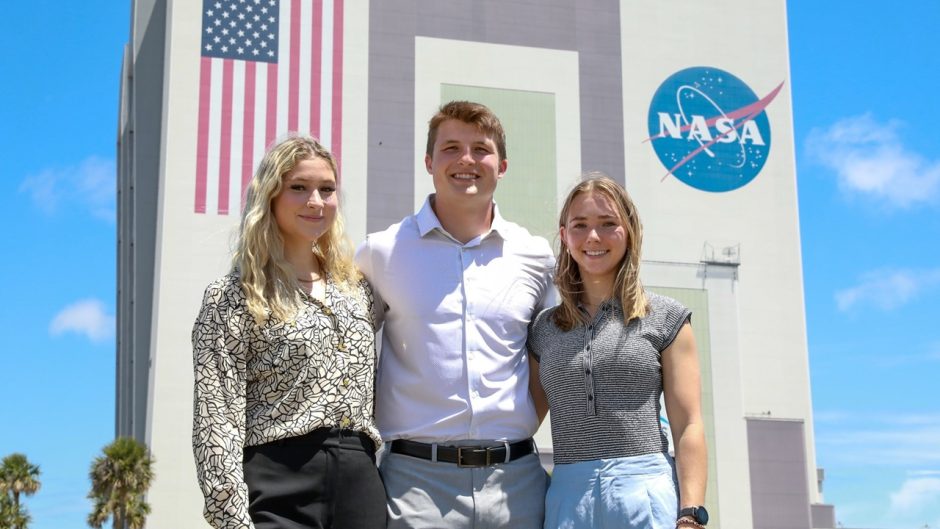 three people standing in front of the vehicle assembly building at NASA