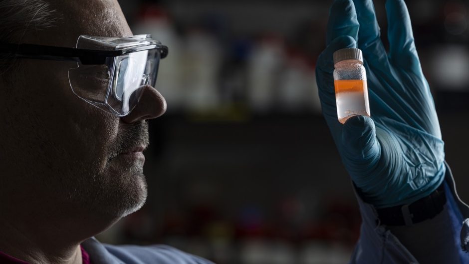 researcher holding a bottle of liquid while looking at it.