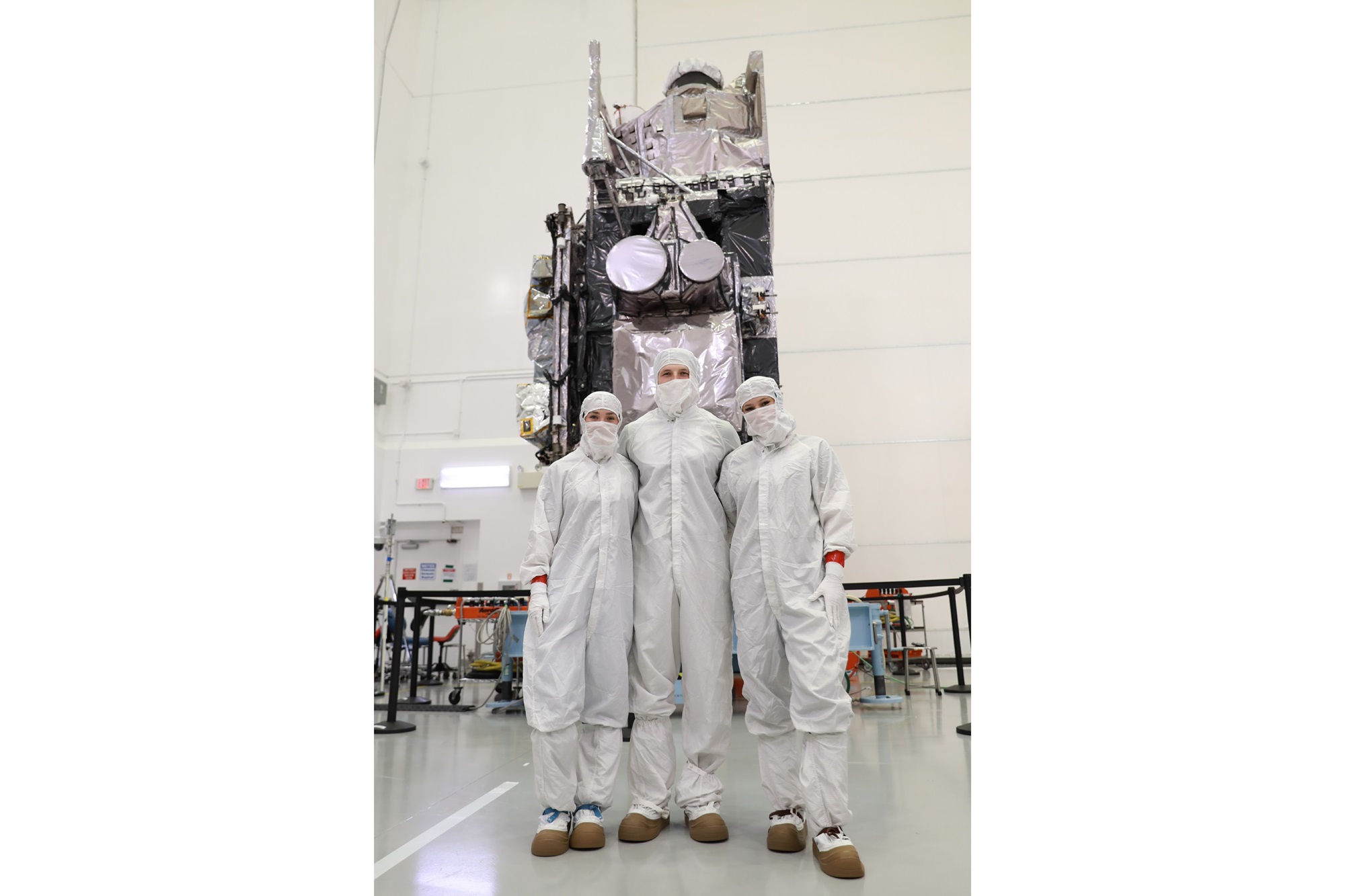 Leah Selm, Jack Meyer and Marina Crownover stand in clean suits in front of a GOES-U satellite that launched from the Kennedy Space Center on June 25.