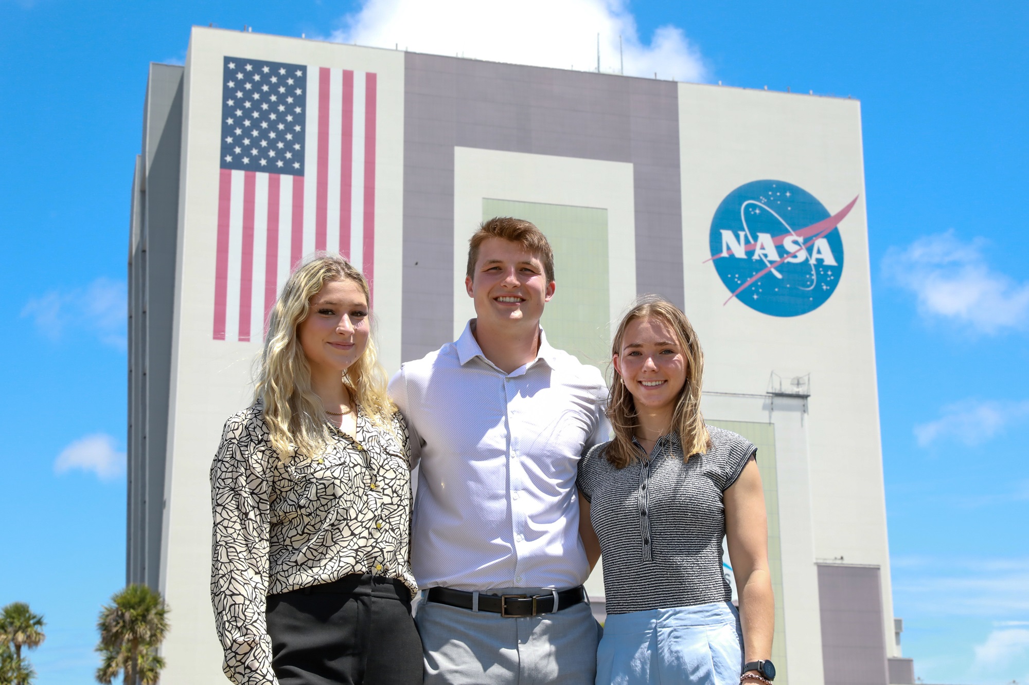 three people standing in front of the vehicle assembly building at NASA