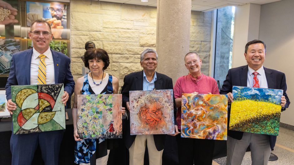 faculty hold paintings and smile