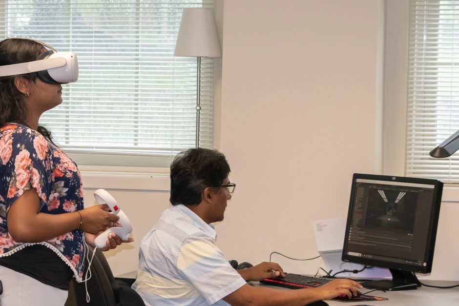 Student wears VR goggles as professor looks at computer screen