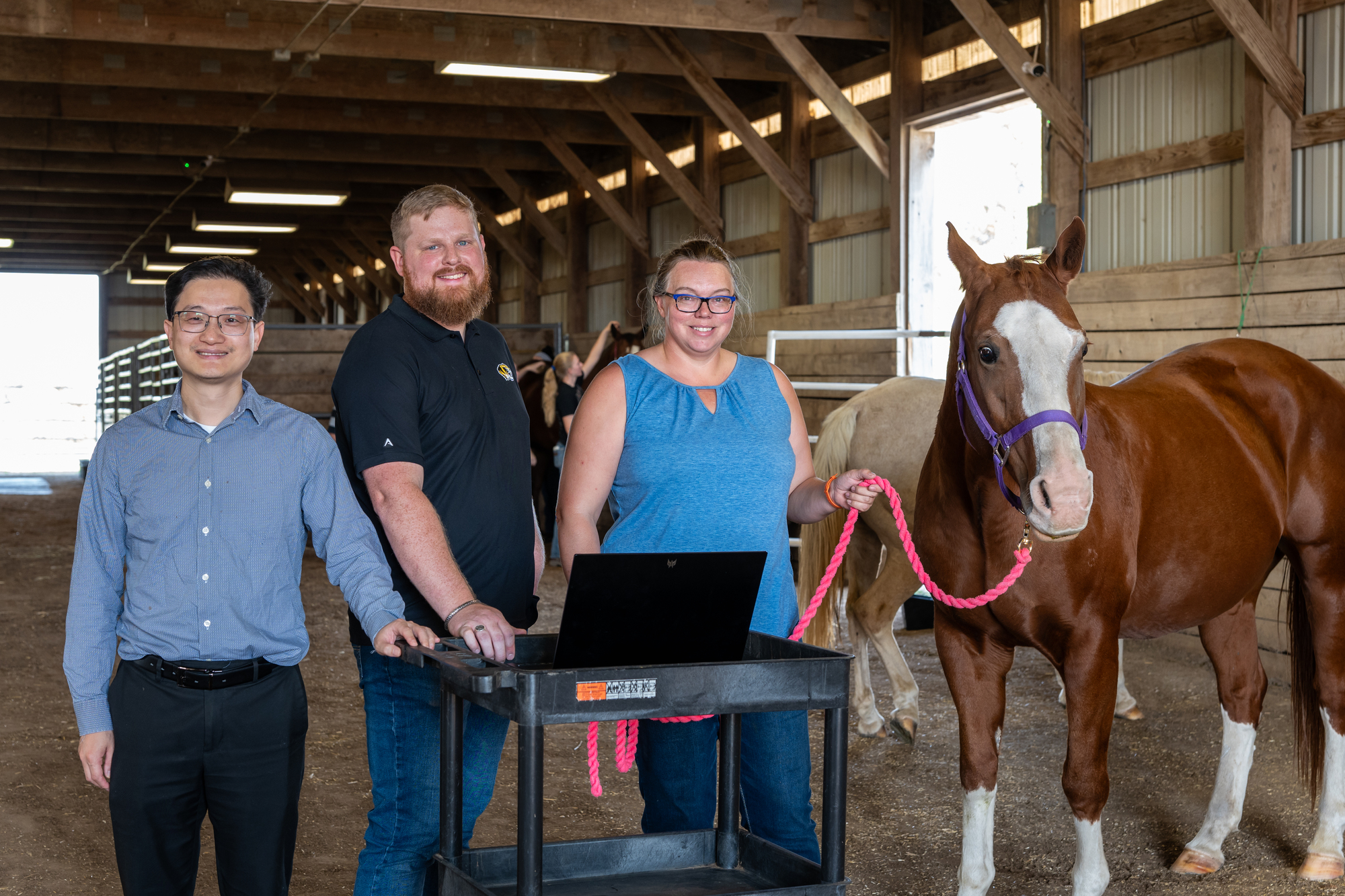 Three people in a barn with a horse