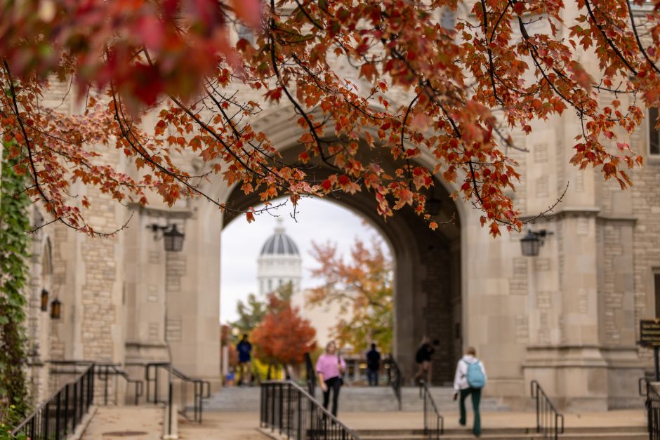 Red leaves hang over white brick building with archway