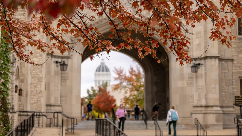 Red leaves hang over white brick building with archway