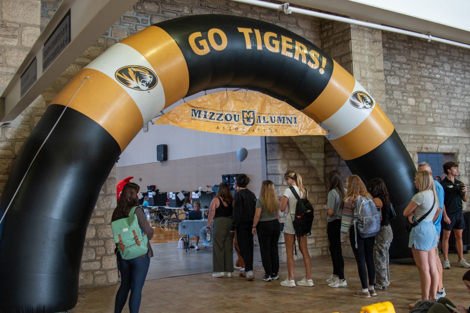 Students wait in line under black and gold arch