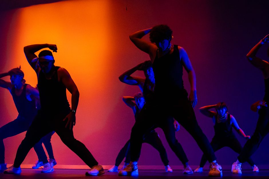 Students dance in front of orange and purple background