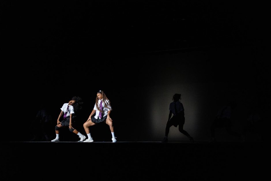 Students in white shirts dance in front of black screen