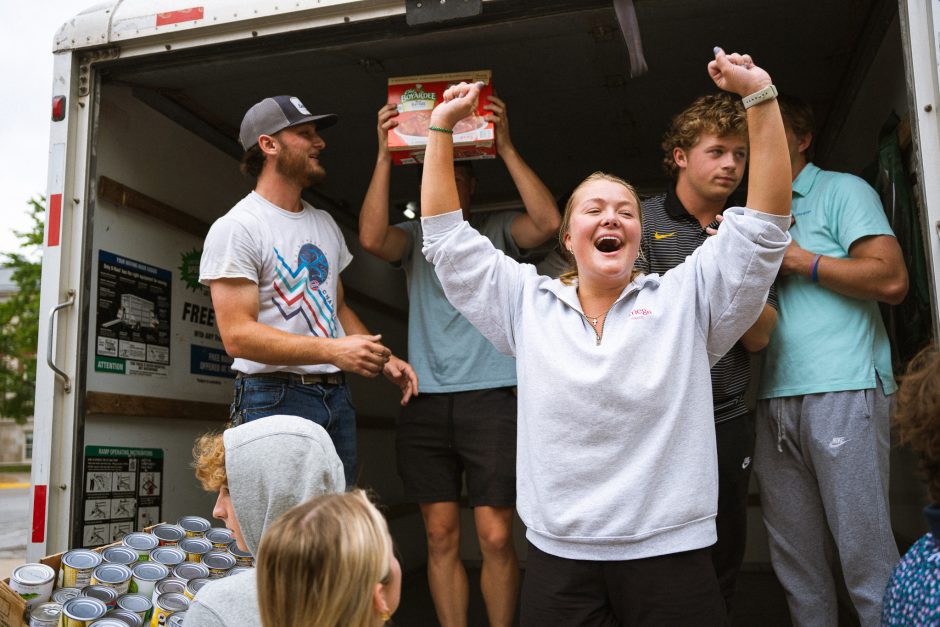 Woman with raised arms with students holding food behind her