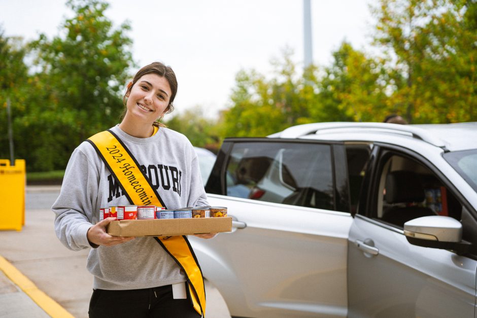 Student smiles at camera holding box of food