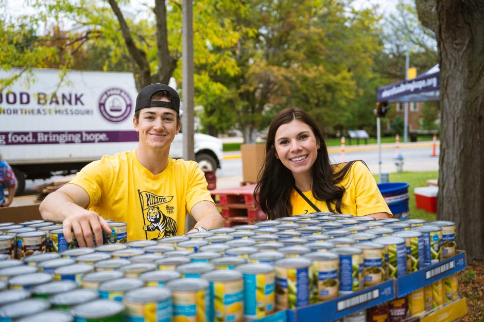 Two students smile at camera behind boxes of food