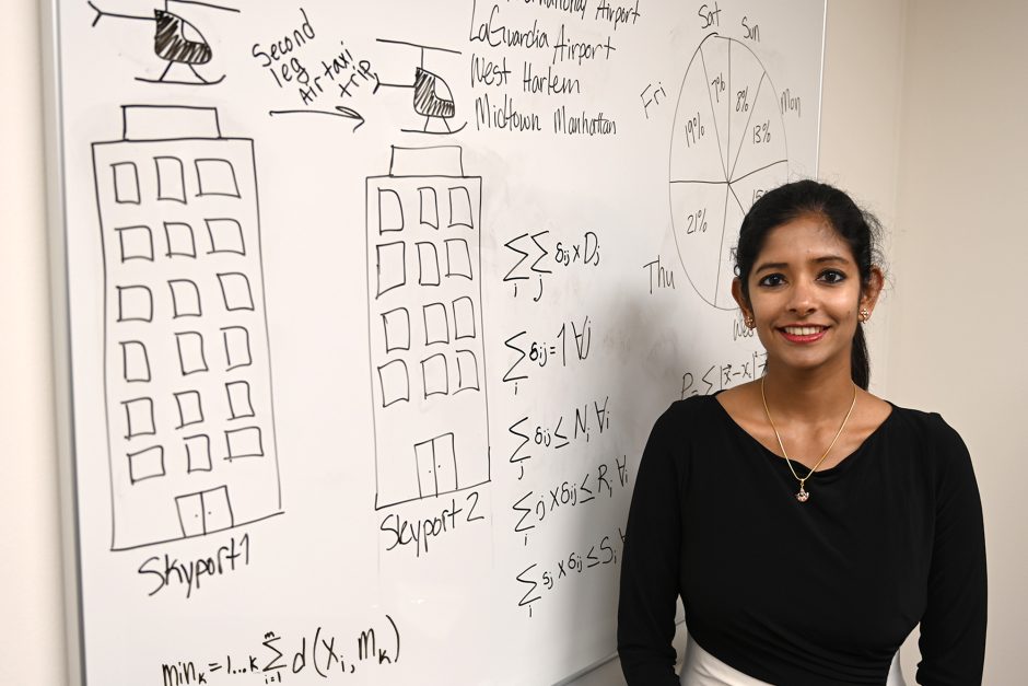 Suchi Rajendran in front of white board with algorithms and sketches