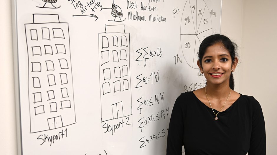 Suchi Rajendran in front of white board with algorithms and sketches