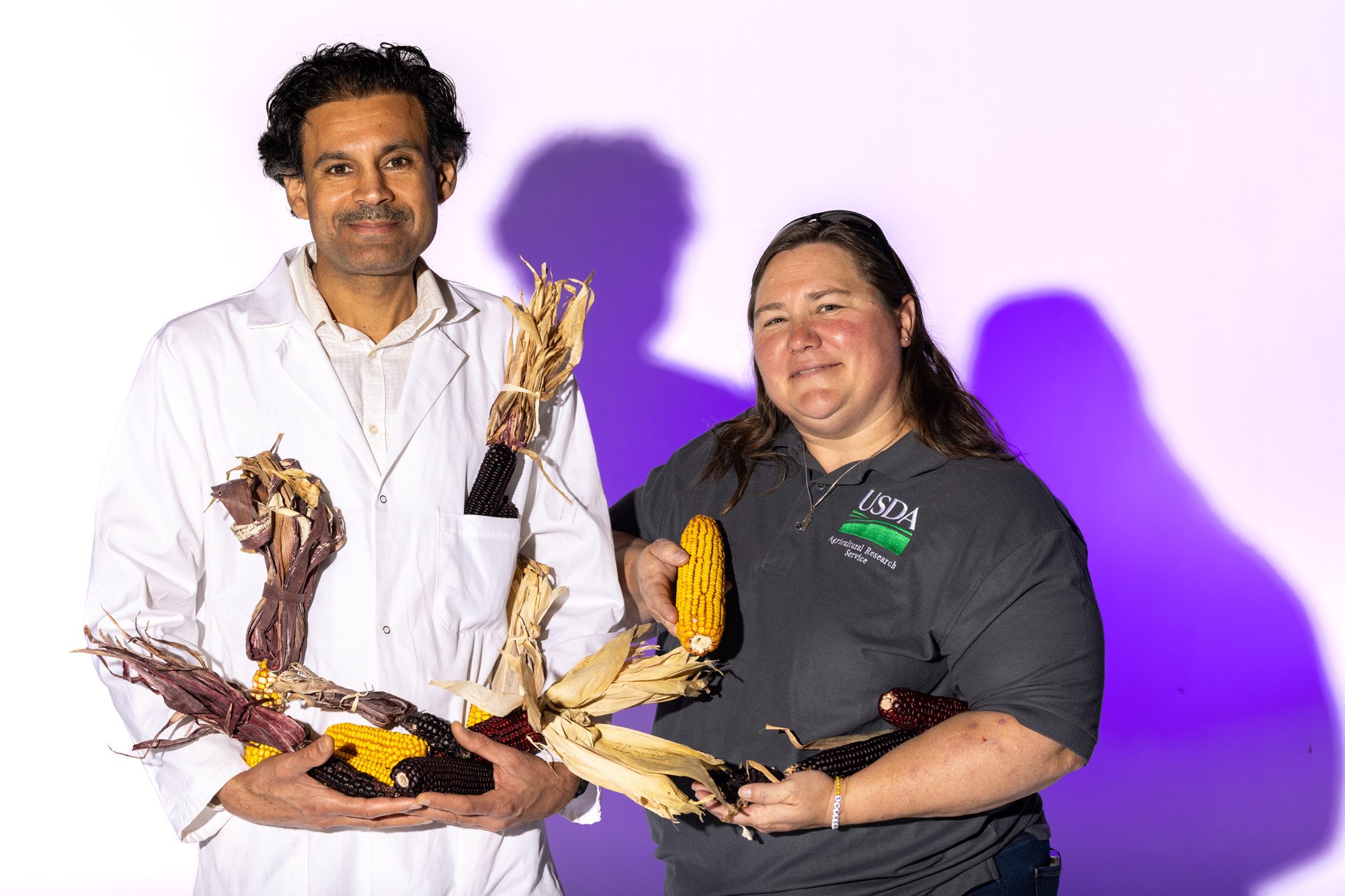 Two people holding different varieties of corn