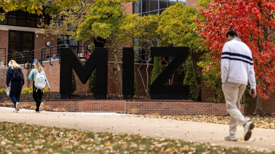 people walk in front of the M-I-Z statue on a fall day