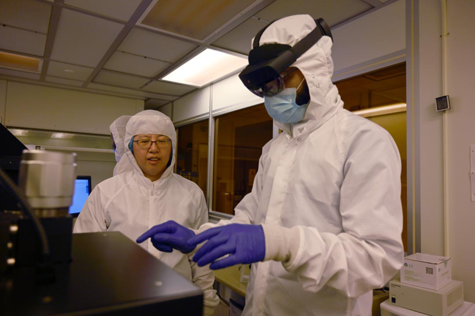 Two people in lab coats and goggles work with materials in lab