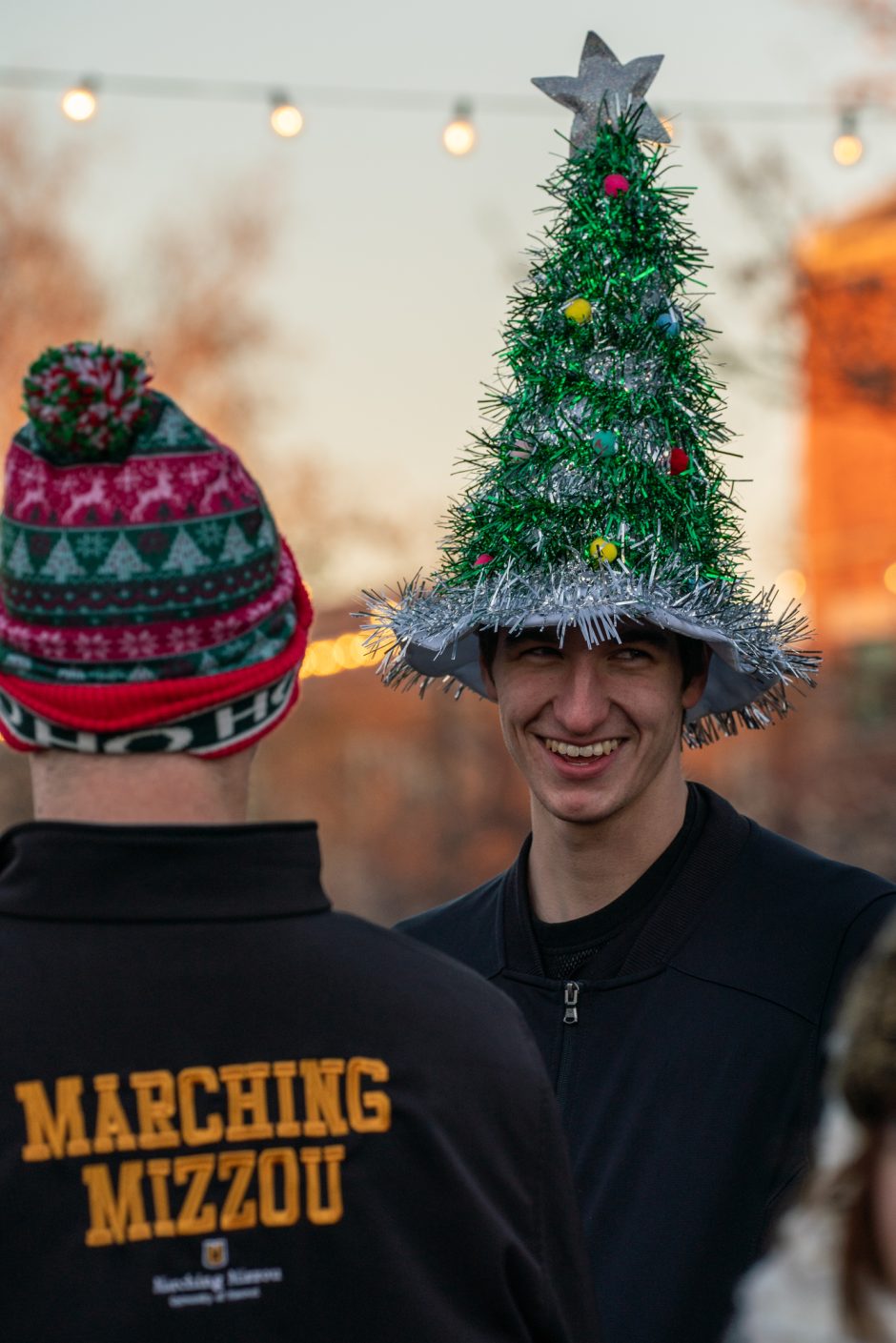 Student wearing a Christmas tree hat smiles at camera