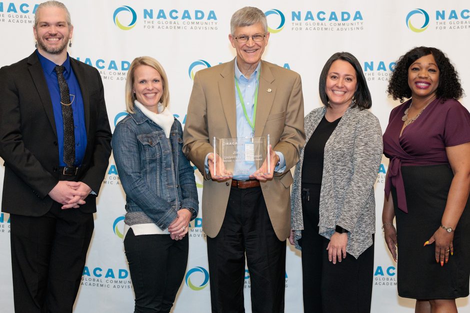 Man holding award surrounded by four people