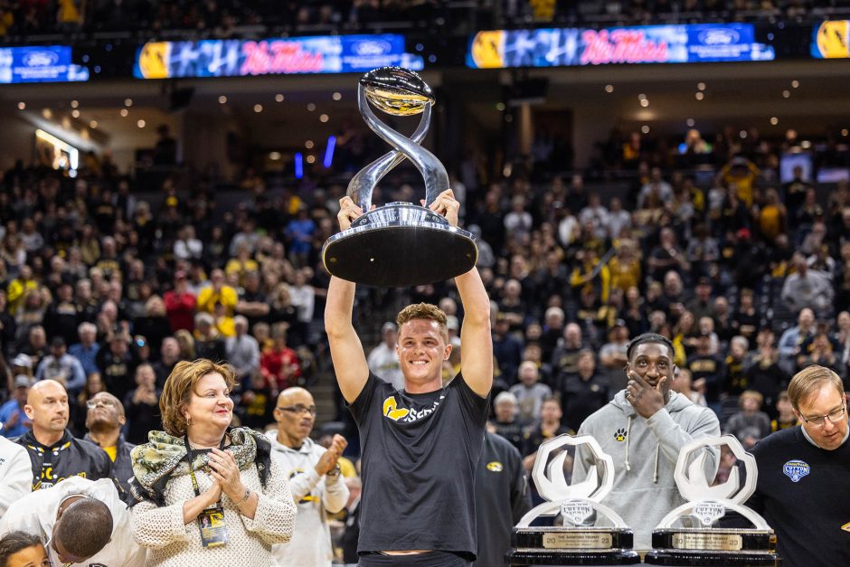 Man holds trophy above head in front of crowd