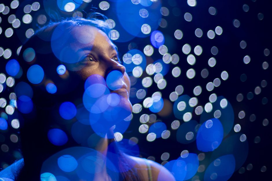 Person surrounded by blue looks up at white lights