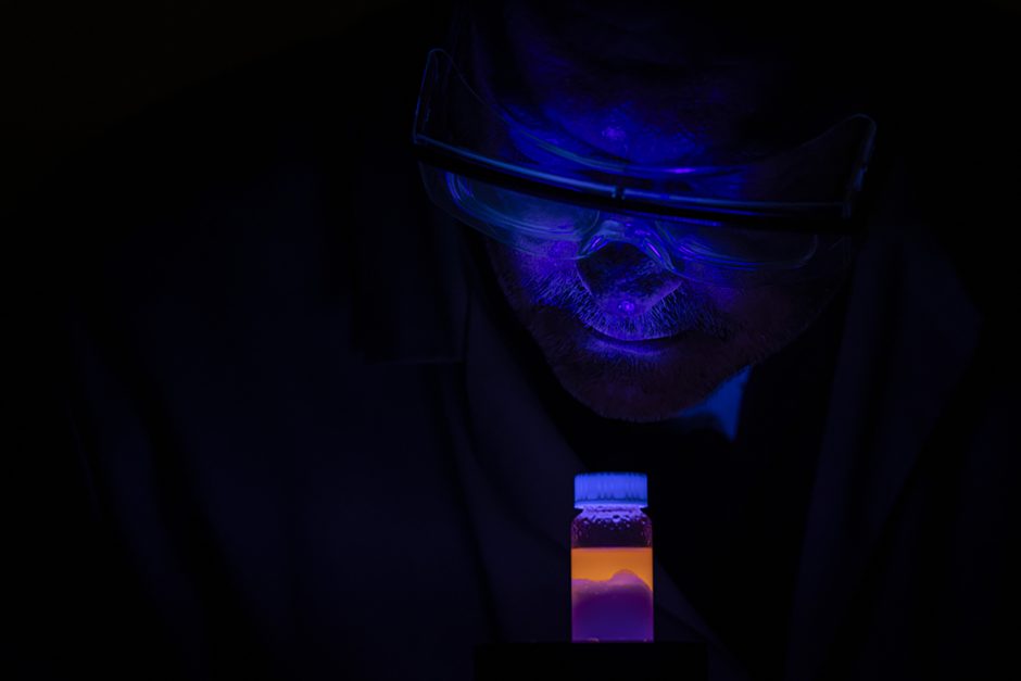 Face illuminated with blue light looks at orange vial