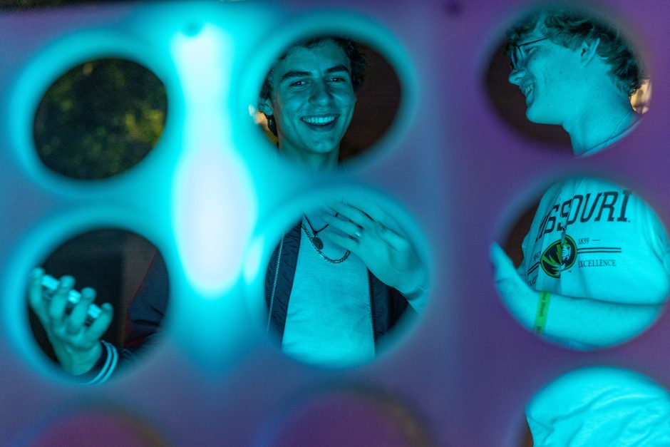 People look through holes illuminated by green and blue lights