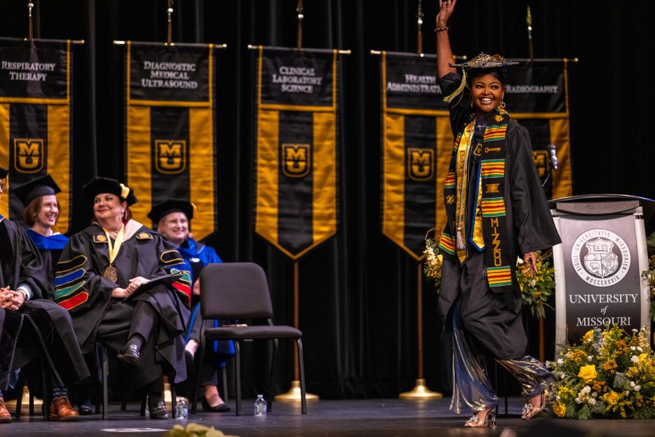 Graduate crosses platform with arm raised