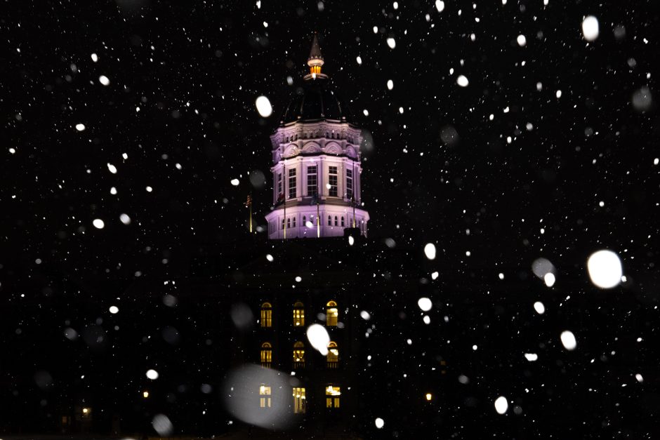 The Jesse Hall spire at night, illuminated by building lights, with snowflakes lit up by a flash falling in the foreground.