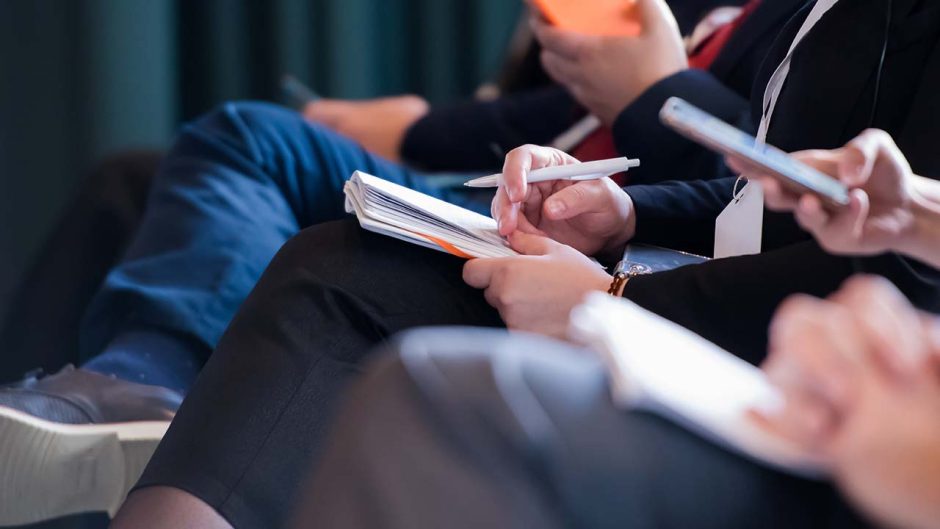 Closeup of people taking notes at a meeting.