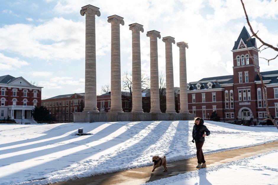 Person walking on sidewalk as sun shines on snowy ground