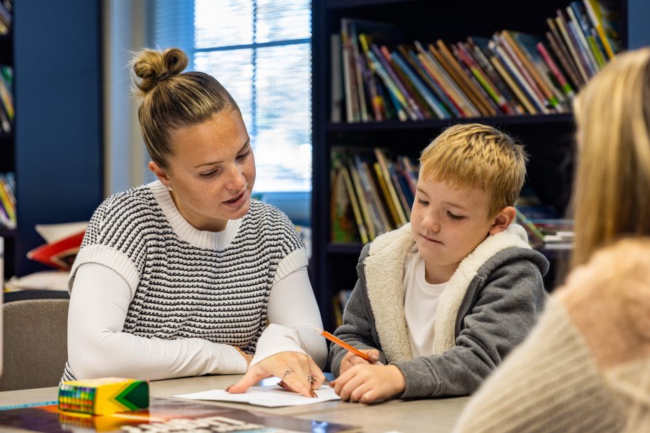 Student works with child at table in front of bookcase