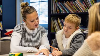 Student works with child at table in front of bookcase