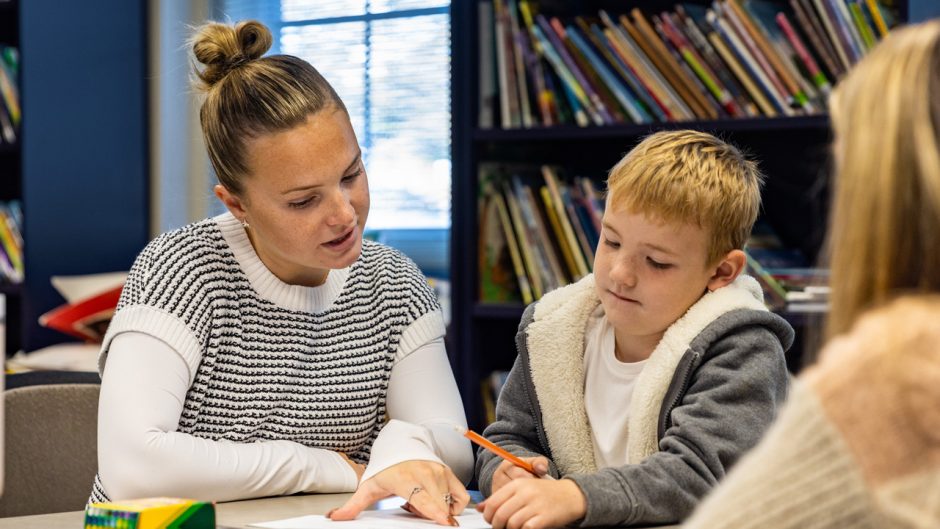 Student works with child at table in front of bookcase