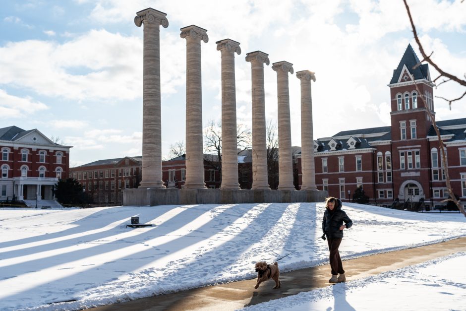 Person walking a dog in front of the Columns on a snowy day
