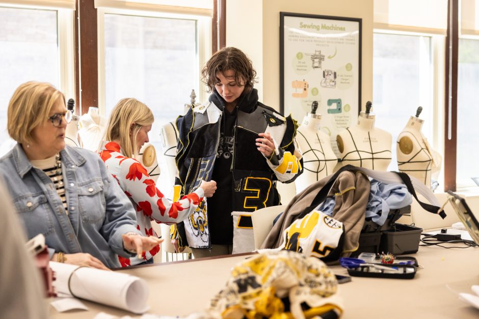 Student holds up clothing as another works on it