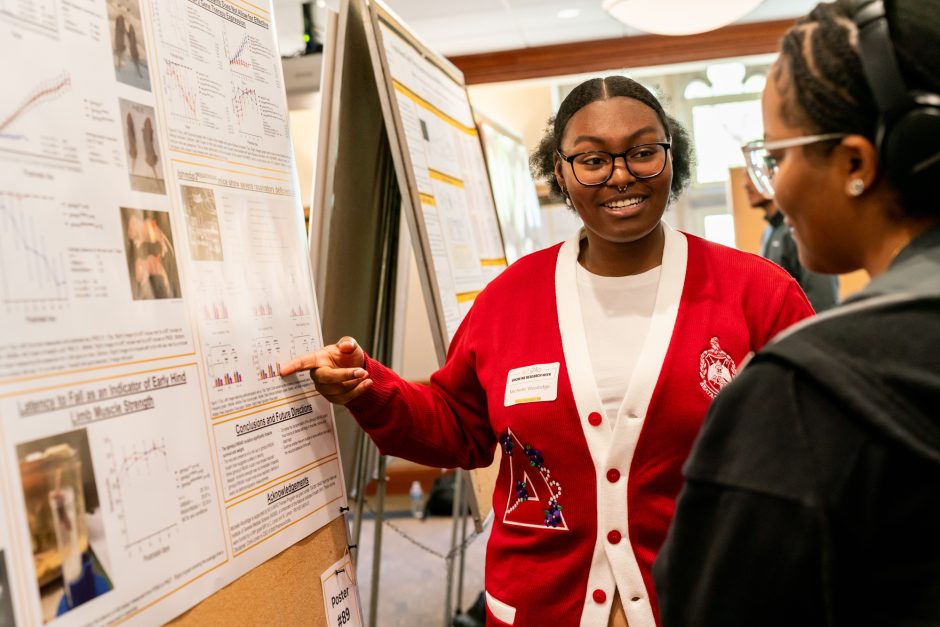 A student pointing to research poster as another person looks on