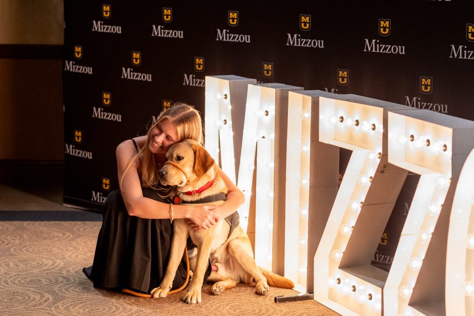 Student hugging a dog in front of an MIZZOU sign