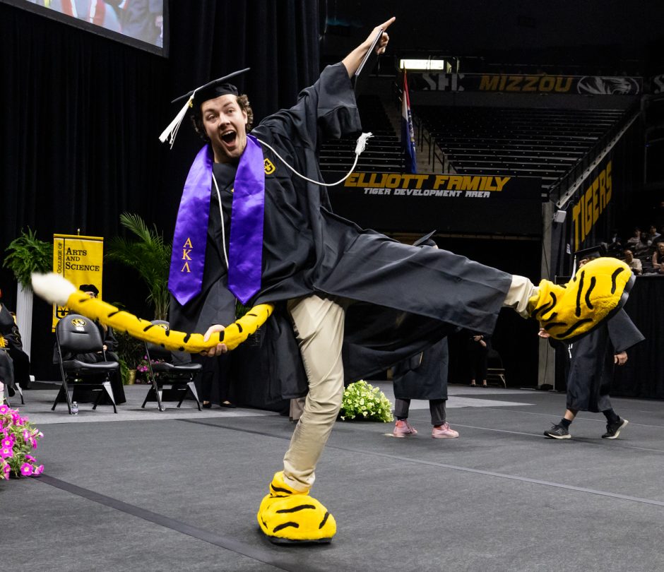 Student in Truman the Tiger feet and tail celebrating at graduation ceremony