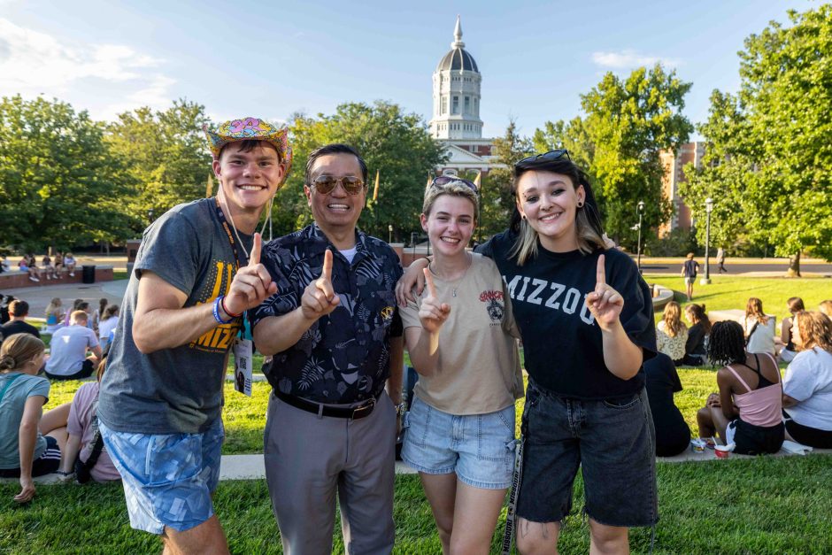 Students and university president holding up index fingers