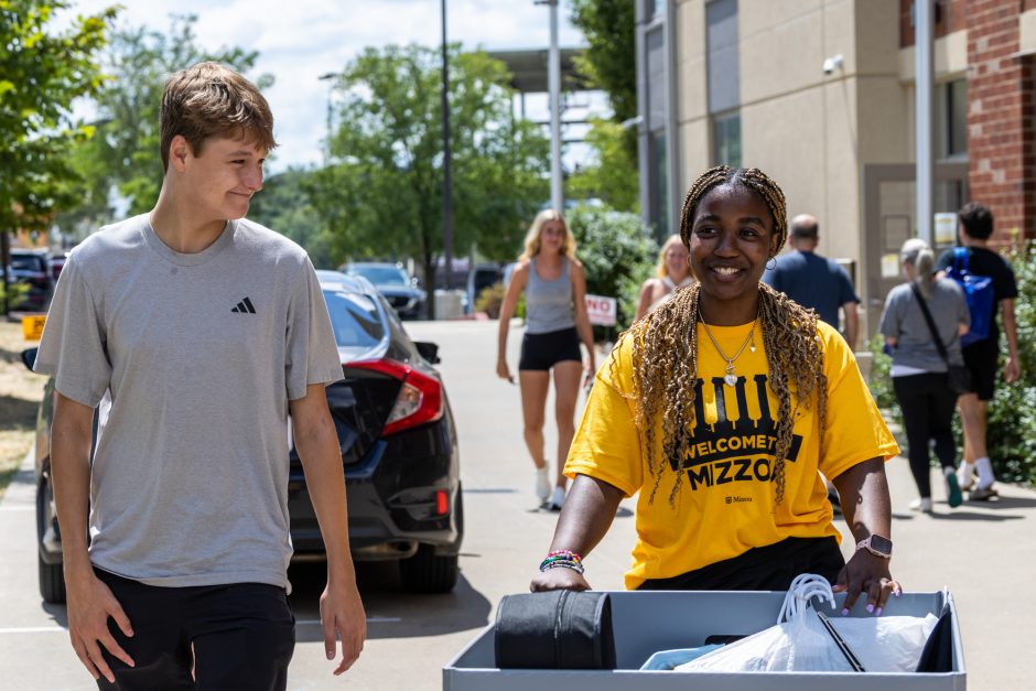 Student helping another by pushing a large bin of possessions at move-in