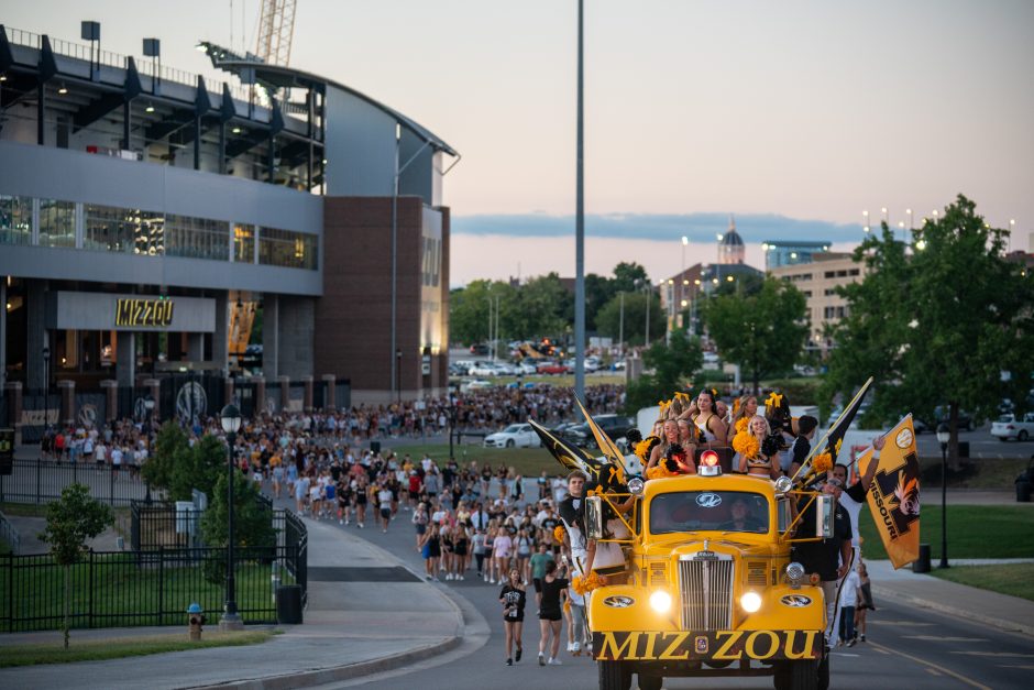 Yellow firetruck with students in the back and others following in the street