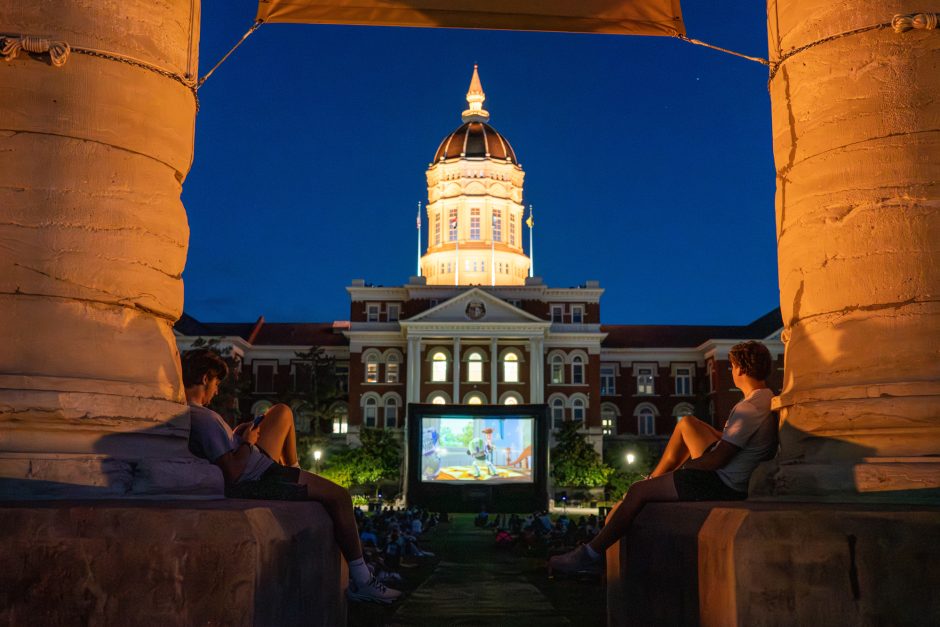 Students watching a movie outside in front of illuminated Jesse Hall