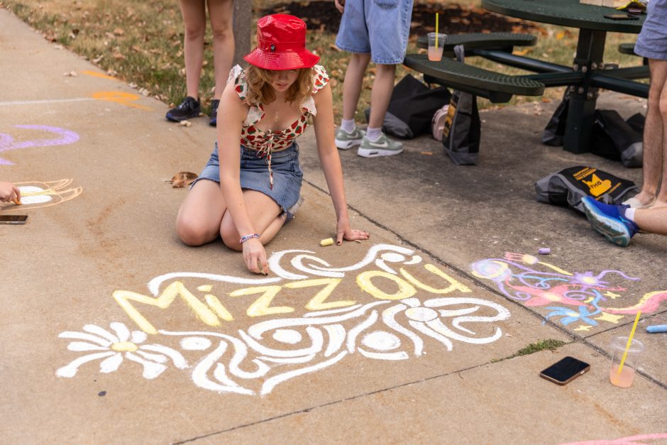 Student writing "Mizzou" on the sidewalk in chalk