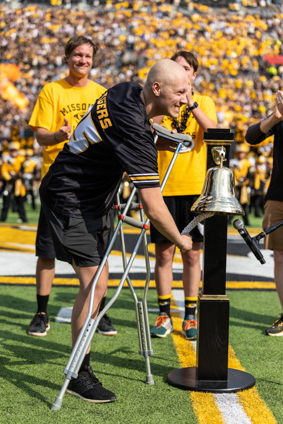 Person wearing football jersey ringing a bell on football field