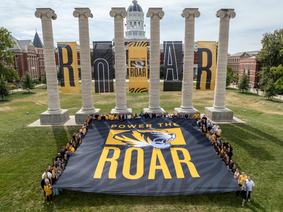 Power the Roar banner held by people in front of the Columns