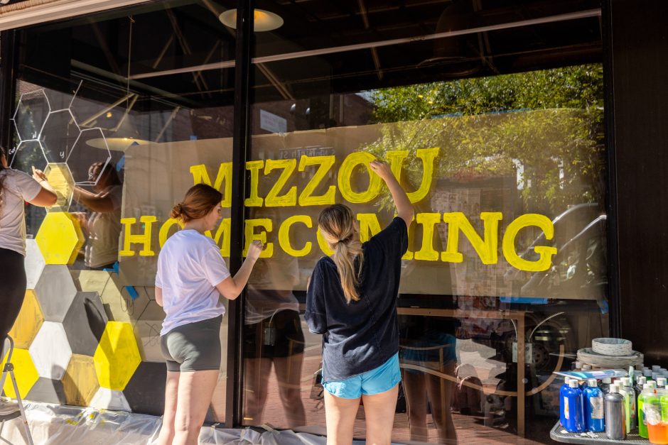 Two students painting a window for homecoming