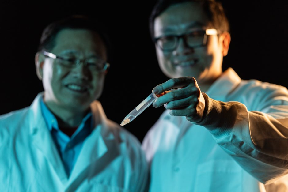 Two researchers in lab coats and one is holding a small vial