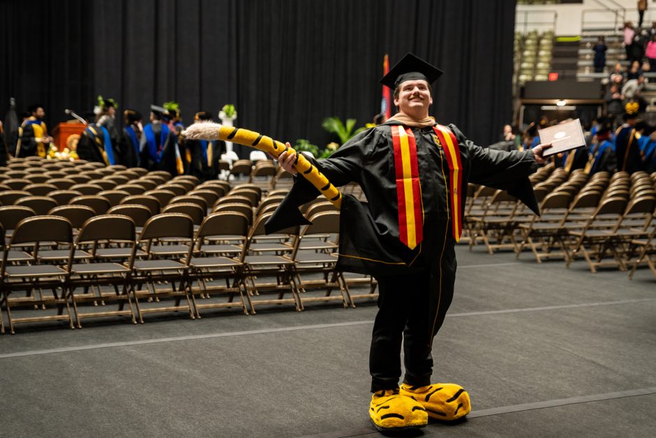 Graduate in cap and gown wearing Truman the Tiger feet and tail