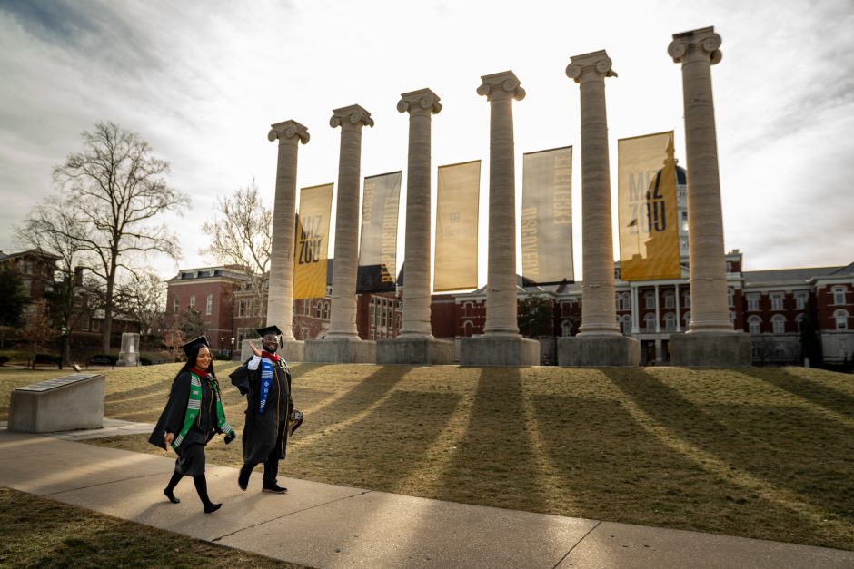 Two graduates in caps and gowns walking in front of the Columns
