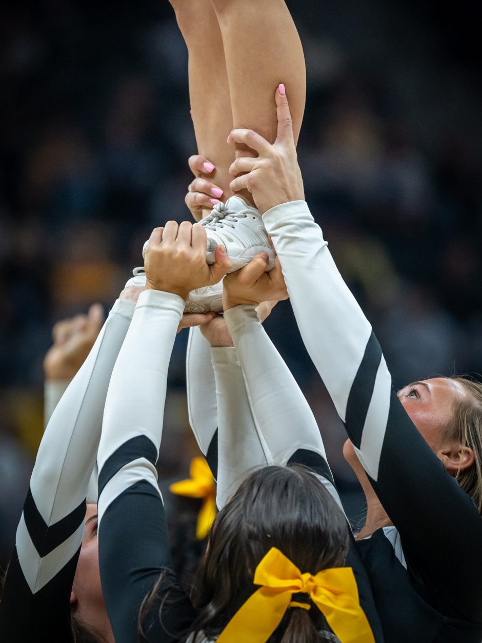 Three Mizzou cheerleaders holding the feet and legs of elevated cheerleader